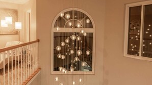 Ein mehrgeschossiges Interieur mit einer Treppe, einer dekorativen Deckenleuchte und einem Fenster mit herunterhängenden Lampen.