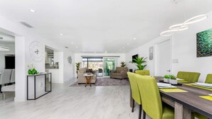 Ein modernes Wohnzimmer mit Essbereich, mit großem Fenster, einer Couch, einem Couchtisch und einem Esstisch mit Stühlen.