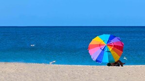Ein Strand mit einem bunten Sonnenschirm und einem klaren, blauen Meer.