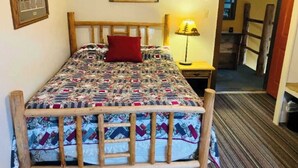 Ein Bett mit einem gemusterten Quilz, einem Holzkopfteil, einem roten Kopfkissen, einer Nachttischlampe und einem Nachttisch aus Holz.