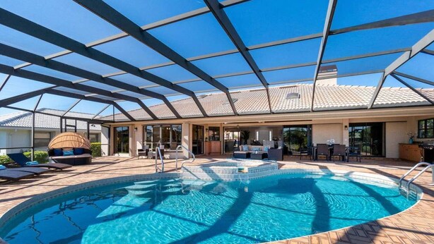 En swimmingpool med glastag, liggestole og et overdækket opholdsområde.