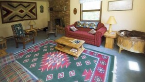 A living room with a red sofa, a wooden coffee table, a patterned rug, a fireplace, and a window with curtains. - Beautiful, Quaint, and Cozy Rooms. (Wolf Creek)