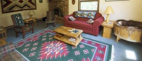 A living room with a red sofa, a wooden coffee table, a patterned rug, a fireplace, and a window with curtains.