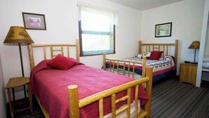 A bedroom with two single beds, a window with blinds, a lamp, and a small table. - Beautiful, Quaint, and Cozy Rooms. (Wolf Creek)