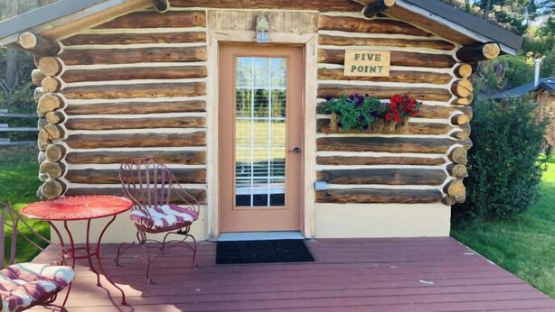 A log cabin with a 'FIVE POINT' sign, a door with a window, two chairs, and a small table on a wooden deck.