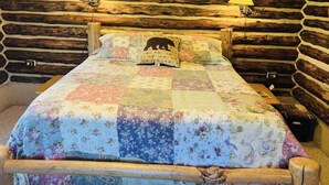 A bed with a floral quilt and a bear-shaped pillow in a log cabin room.