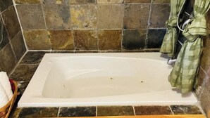 A bathroom with a white bathtub, a tiled wall, and a green towel hanging on the wall.