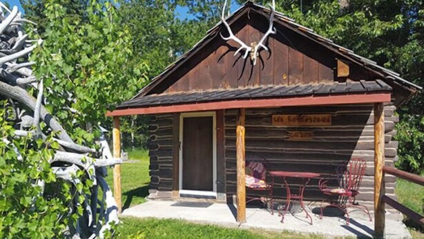 Una cabana rústica de fusta amb un porxo, una porta i un rètol que diu "Life Homestead".