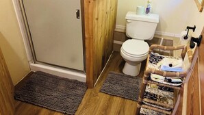 A bathroom with a shower, toilet, and a wicker basket with toiletries. - Beautiful and Quaint Cabin  (Wolf Creek)