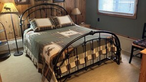 A bed with a metal frame, a quilt, and a nightstand with a lamp. - Beautiful and Quaint Cabin  (Wolf Creek)