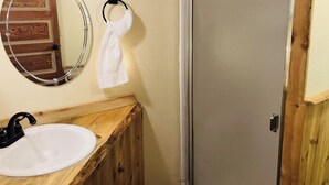 A bathroom with a wooden vanity, a white sink, a mirror, and a towel hanging on a towel ring. - Beautiful and Quaint Cabin  (Wolf Creek)