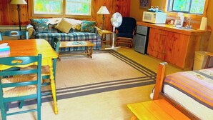 A cozy cabin-style room with a sofa, a dining table, a kitchen area with a microwave, and a fan. - Beautiful and Quaint Cabin  (Wolf Creek)