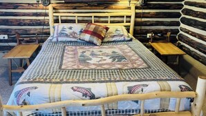 Een bed met een sprei met vismotieven, een houten hoofdbord en twee nachtkastjes met lampen.