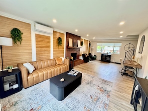 A modern living room with a leather sofa, a black coffee table, a fireplace, and a dining area with a wooden table and chairs.