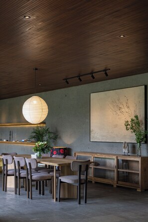 Ein stilvoller Essbereich mit Holztischen und -stühlen, einem großen abstrakten Gemälde an der Wand und einer hängenden Leuchte.