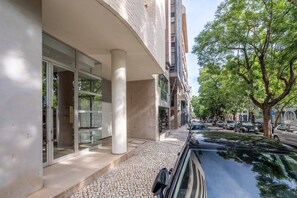 A modern building with a glass facade, a cobblestone pathway, and a tree-lined street. - Spacious Saldanha Flat w/ Private Deck, Near Metro (Lisboa)