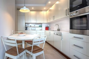 A modern kitchen with white cabinets, stainless steel appliances, and a round dining table with chairs. - Spacious Saldanha Flat w/ Private Deck, Near Metro (Lisboa)