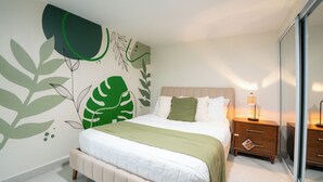 Ein Schlafzimmer mit einem Bett, einem Nachttisch, einer Lampe und einer Wand mit Blattmustern.