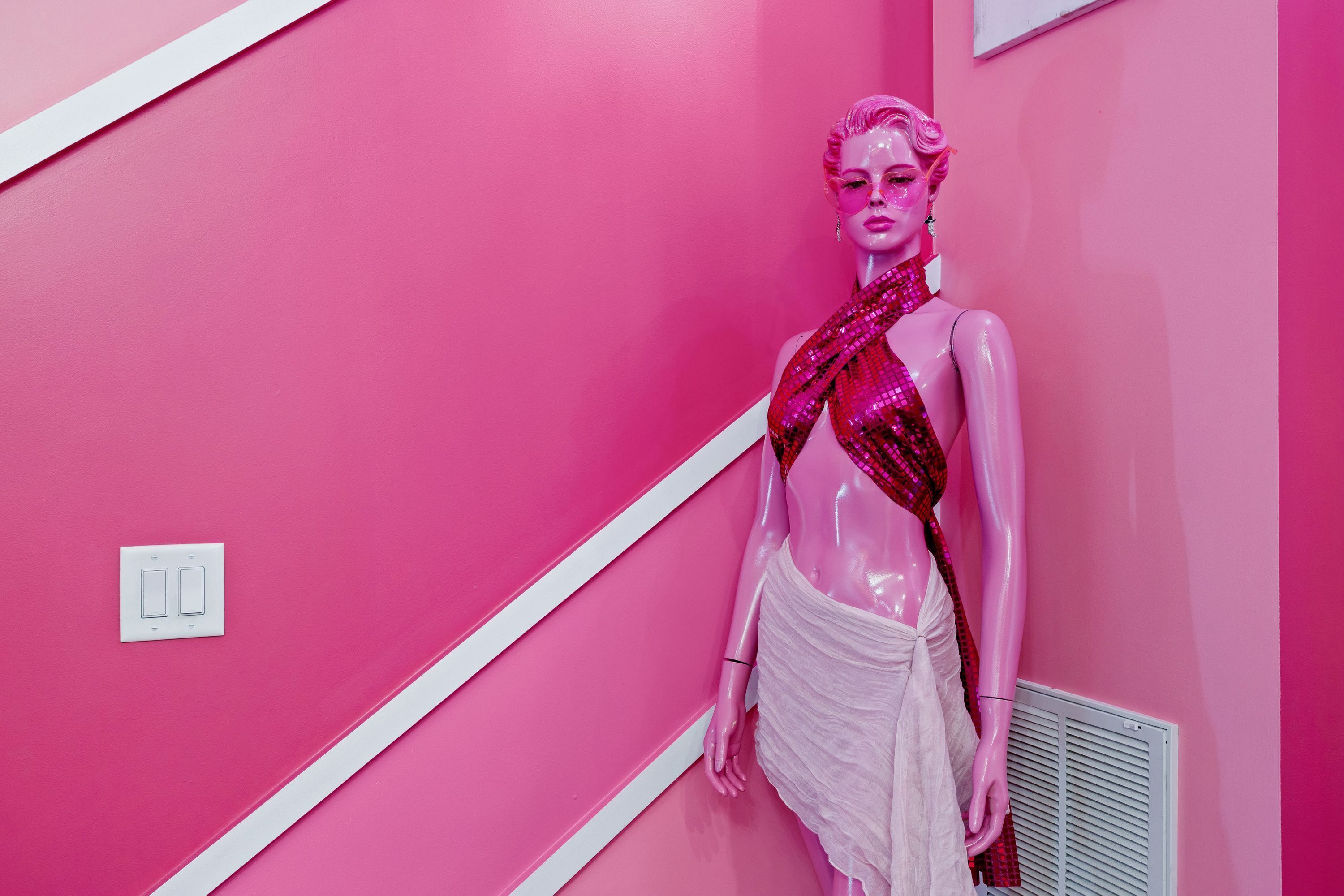 A mannequin in a pink room with white trim and a vent.