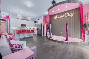 A modern interior with a kitchen, a seating area, and a stage with a sign reading 'Music City'. - Barbie s Nashville Bachelorette Bash (Nashville)