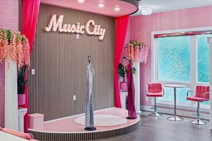 Ein Raum mit einer Bühne, rosafarbenen Stühlen, einem großen Schild mit der Aufschrift 'Music City' und einem Fenster mit Aussicht.
