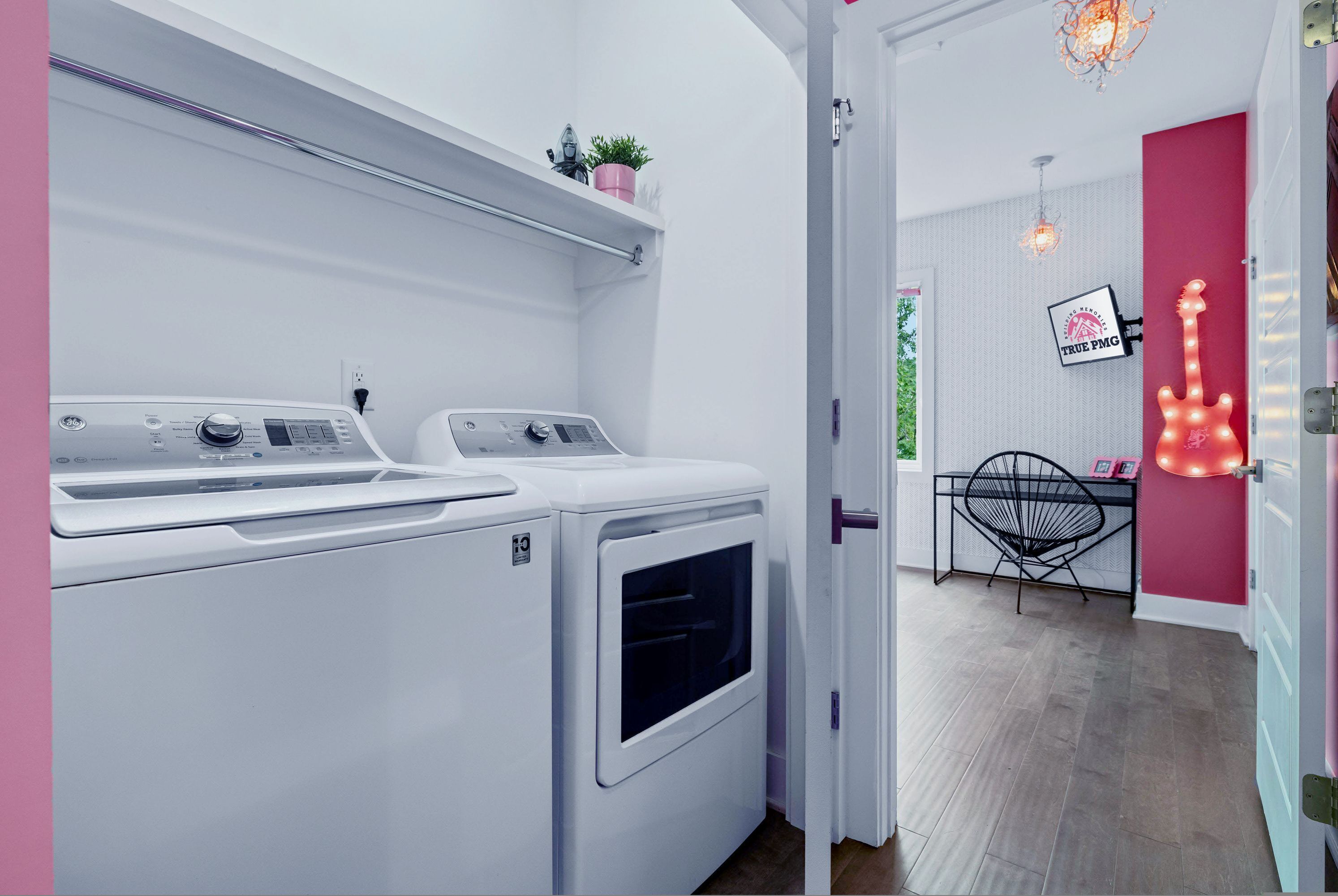 A laundry room with two washing machines, a small shelf with a plant, a chair, and a guitar-shaped light fixture.