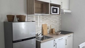 Une cuisine moderne équipée d’un réfrigérateur en acier inoxydable, de meubles blancs, d’un four à micro-ondes et d’une planche à découper en bois.