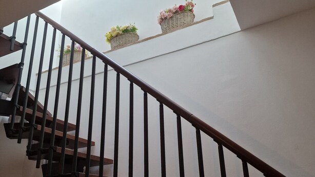 Un escalier doté d’une rampe et de marches en bois mène à un palier. Sur ce palier, on trouve deux paniers en osier remplis de fleurs.