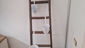 Une étagère en bois, en forme d’échelle, avec trois seaux blancs adossés à un mur blanc.