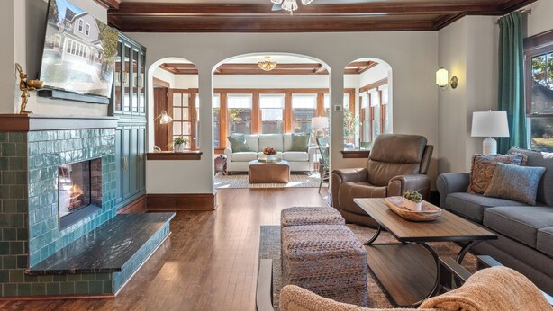 A spacious living room with a fireplace, a ceiling fan, and a view of the backyard through an archway. - Walk to Beach & Pier | Fully-Loaded Kitchen (Sheboygan)