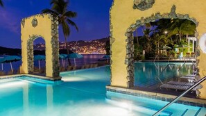 Un área de piscina con arcos de piedra, sillones de descanso y sombrillas.