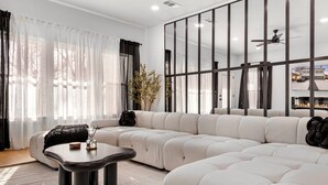 A modern living room with a sectional sofa, a coffee table, and a large window with sheer curtains. - 6BD Duplex, Modern, Lux, Free Park, Pool Table (Dallas)