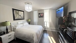 A hotel room with a large bed, bedside lamps, a television, a dresser, and artwork on the walls. - Effortless Downtown Calgary Executive Condo | 6 to 8 Month Occupancy | $1,980/mo (Calgary)