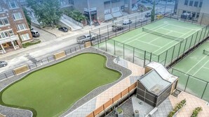 A tennis court with a surrounding fence, a small pool, and a building with a brick facade. - Effortless Downtown Calgary Executive Condo | 6 to 8 Month Occupancy | $1,980/mo (Calgary)
