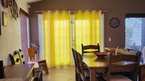 Uma sala de jantar com mesa e cadeiras, um ventilador de teto e uma janela com persianas.