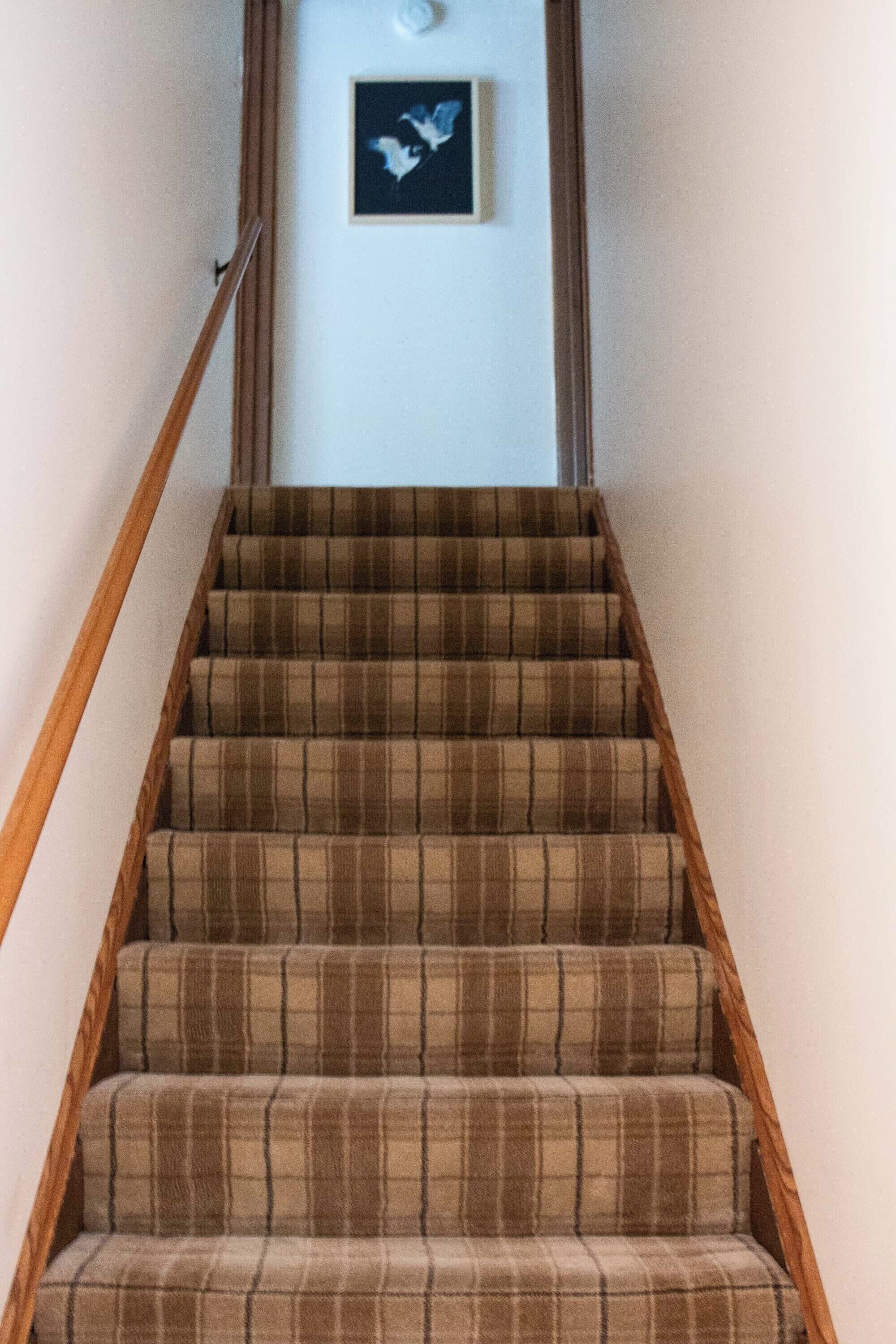 A staircase with a wooden handrail and plaid carpeted steps.