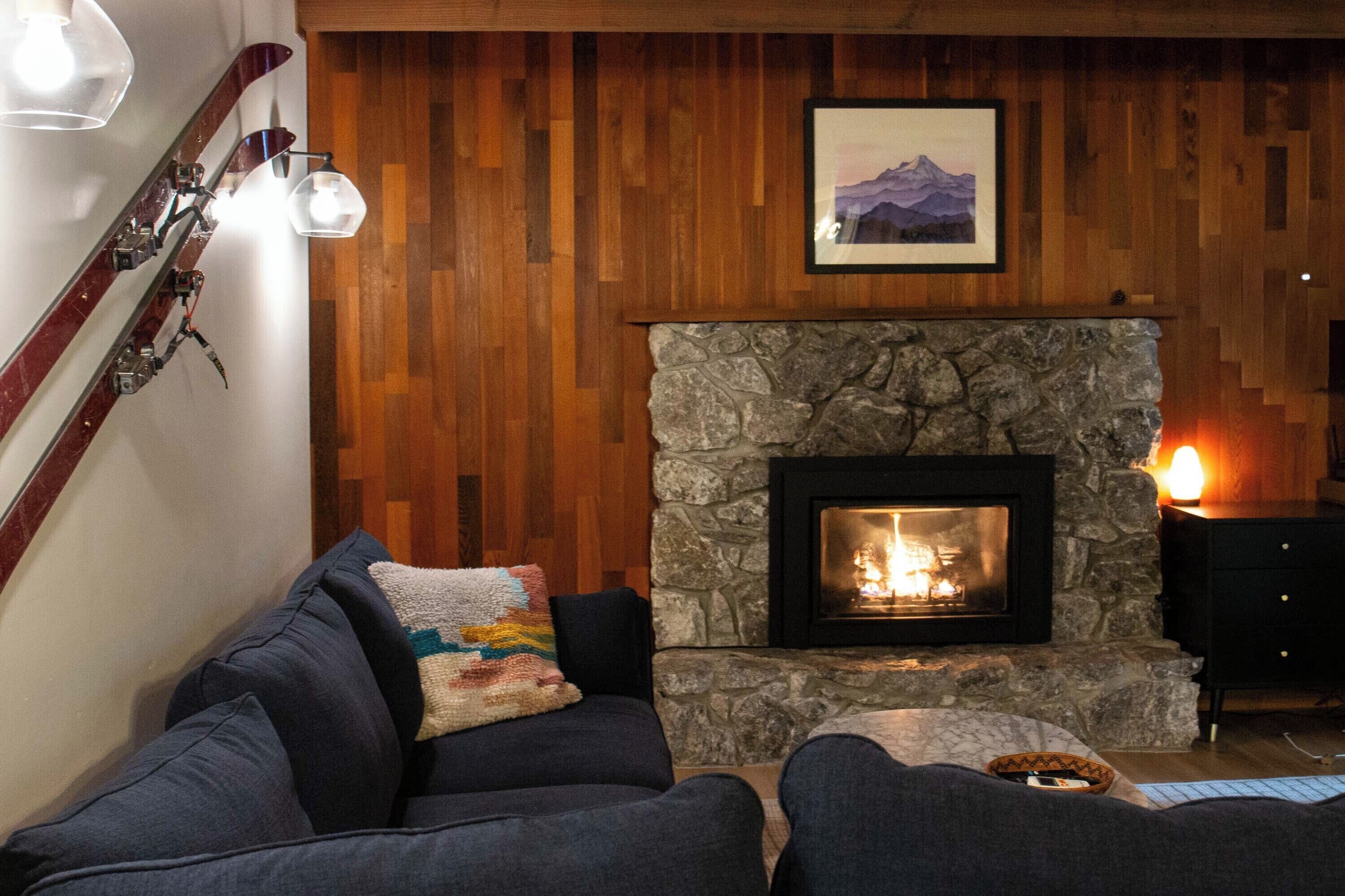 A cozy living room with a stone fireplace, wooden paneling, and a ski rack.