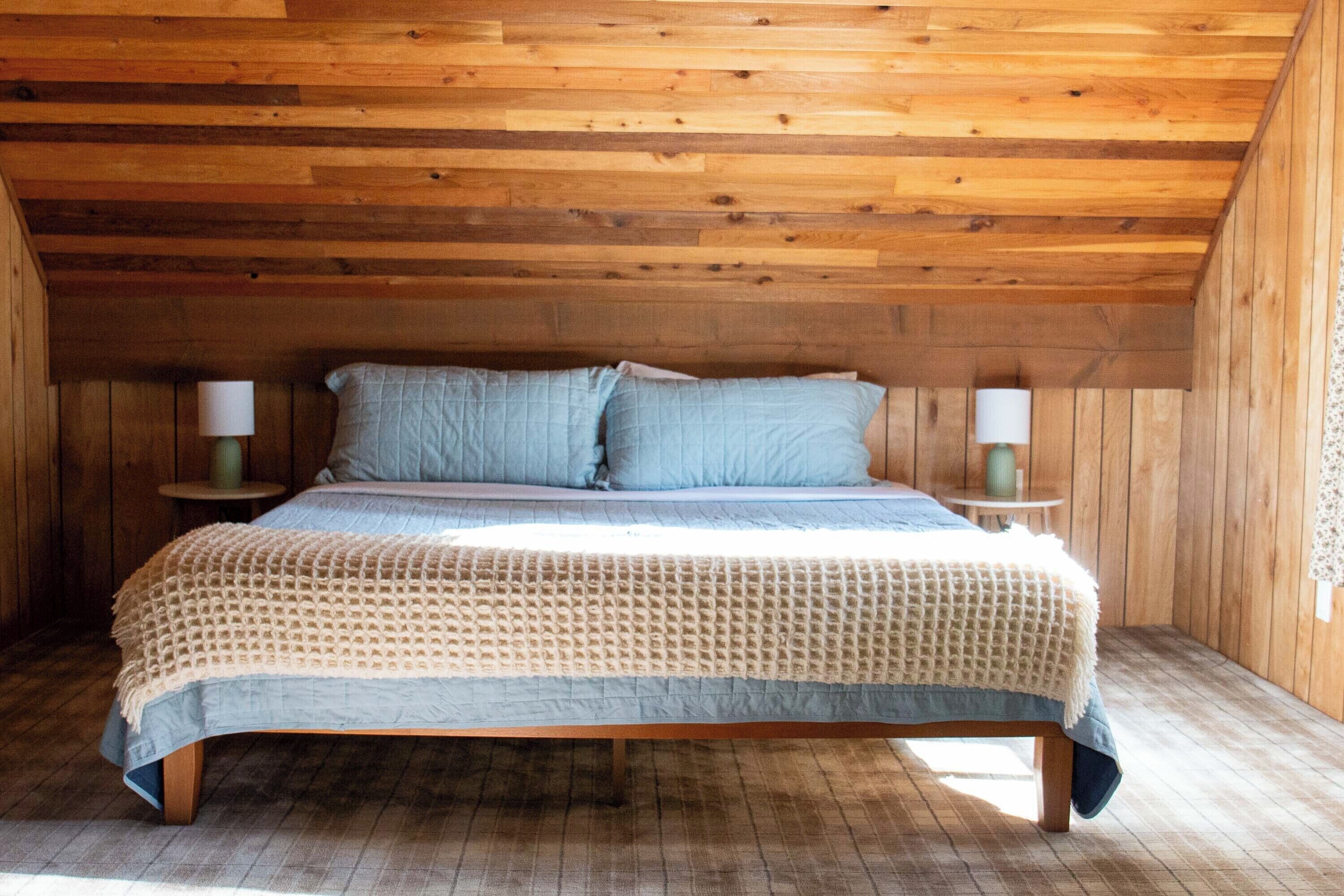 Un dormitorio con paneles de madera, una cama, dos mesitas de noche y un ventanal.