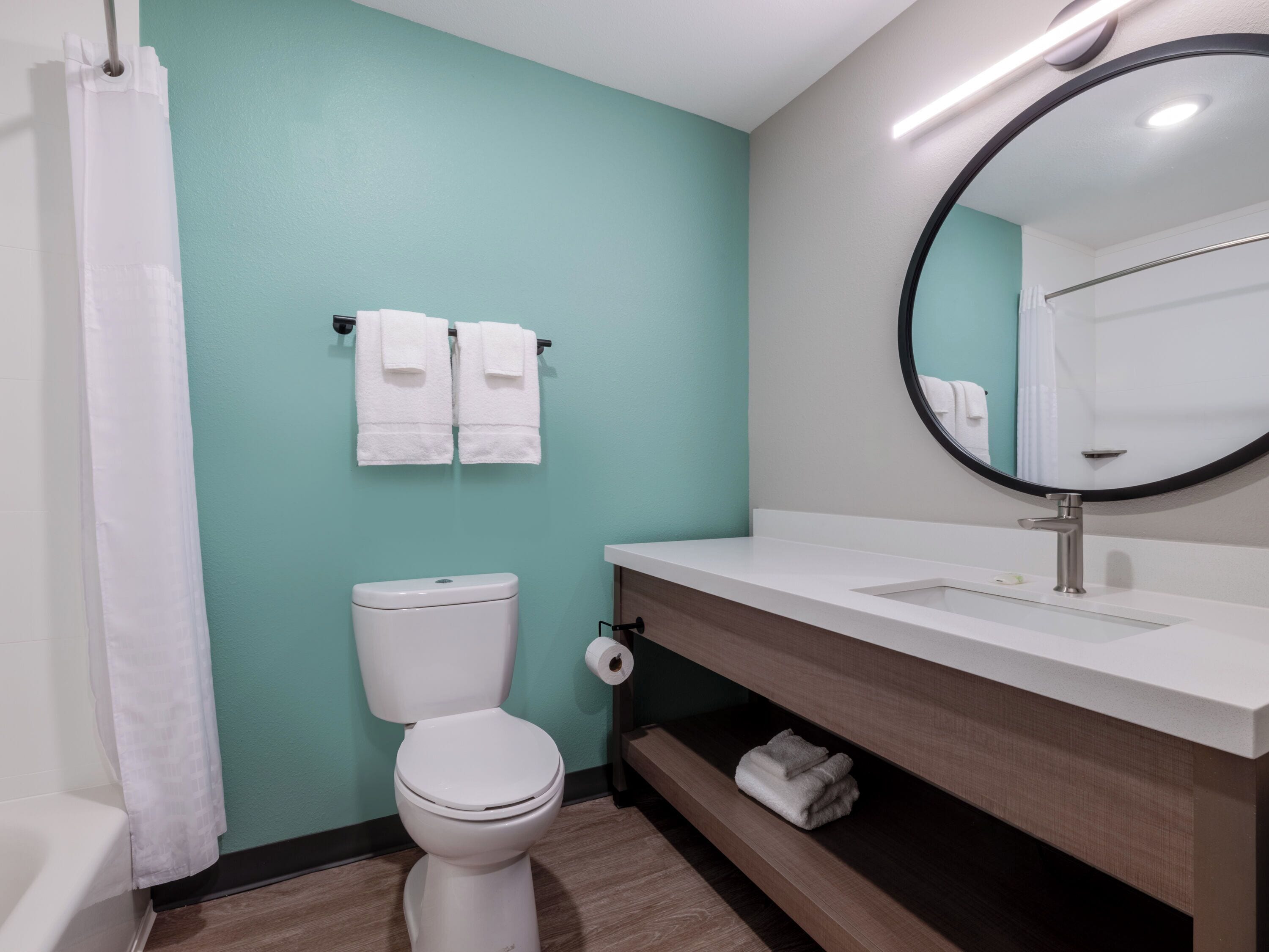A modern bathroom with a toilet, sink, and mirror. There are two towels hanging on the wall.