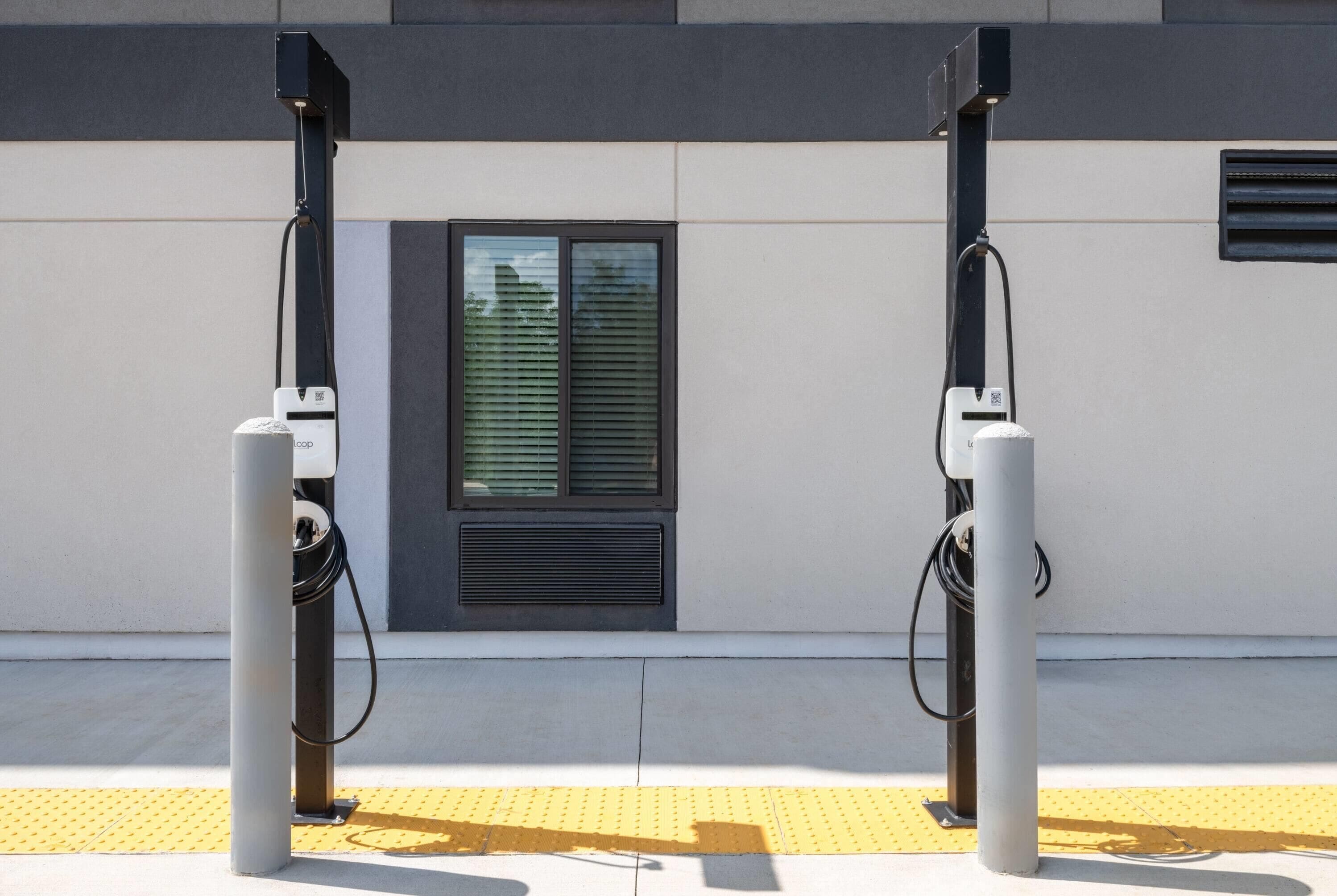 Two electric vehicle charging stations mounted on a building facade with a window and ventilation grilles.