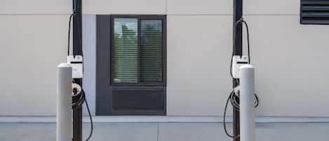 Two electric vehicle charging stations mounted on a building facade with a window and ventilation grilles.