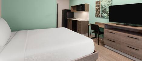 Un dormitorio con cama, escritorio, televisor y kitchenette.