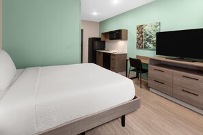 Een slaapkamer met een bed, een bureau, een televisie en een kitchenette.