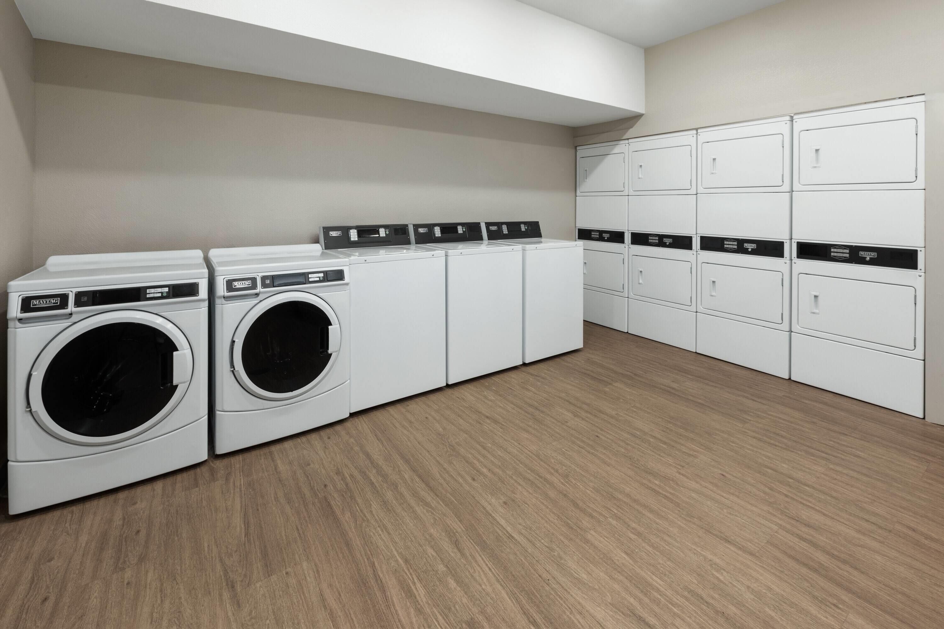 A laundry room with two front-loading washers and dryers, a row of cabinets, and a wooden floor.