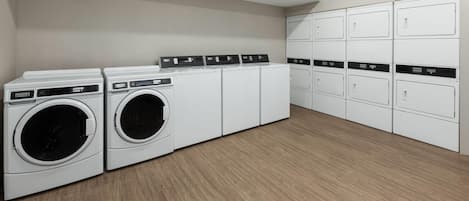 Une buanderie équipée de deux machines à laver et de deux sèche-linge à chargement frontal, d’une rangée de placards et d’un plancher en bois.