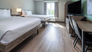 Et hotelværelse med to senge, et skrivebord, et fjernsyn og et vindue med gardiner.