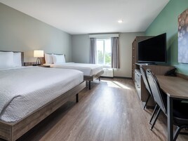 A hotel room with two beds, a desk, a TV, and a window with curtains.