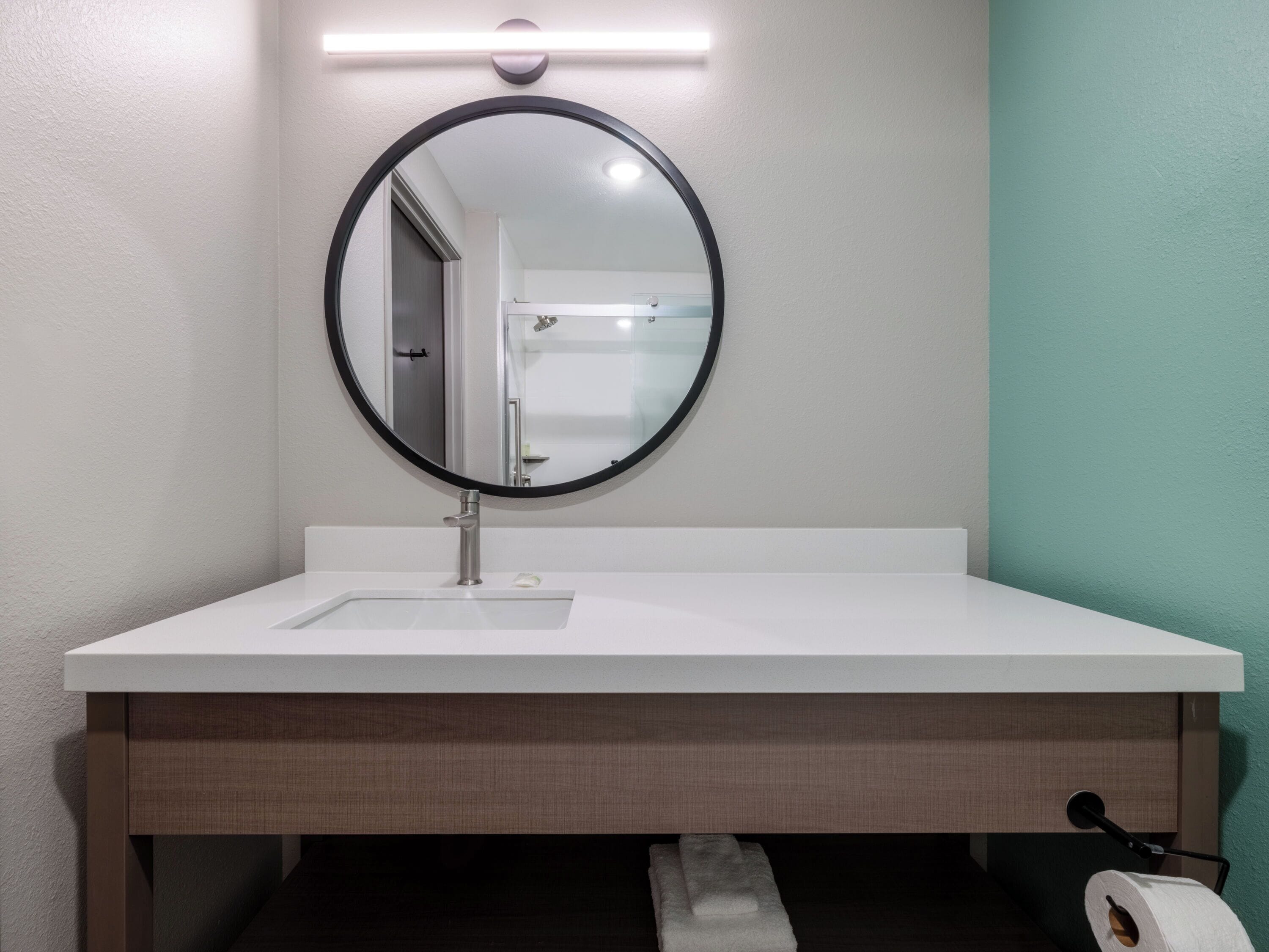 A bathroom with a white sink, a round mirror, and a towel dispenser.