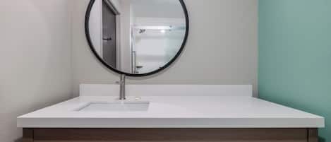 A bathroom with a white sink, a round mirror, and a towel dispenser.