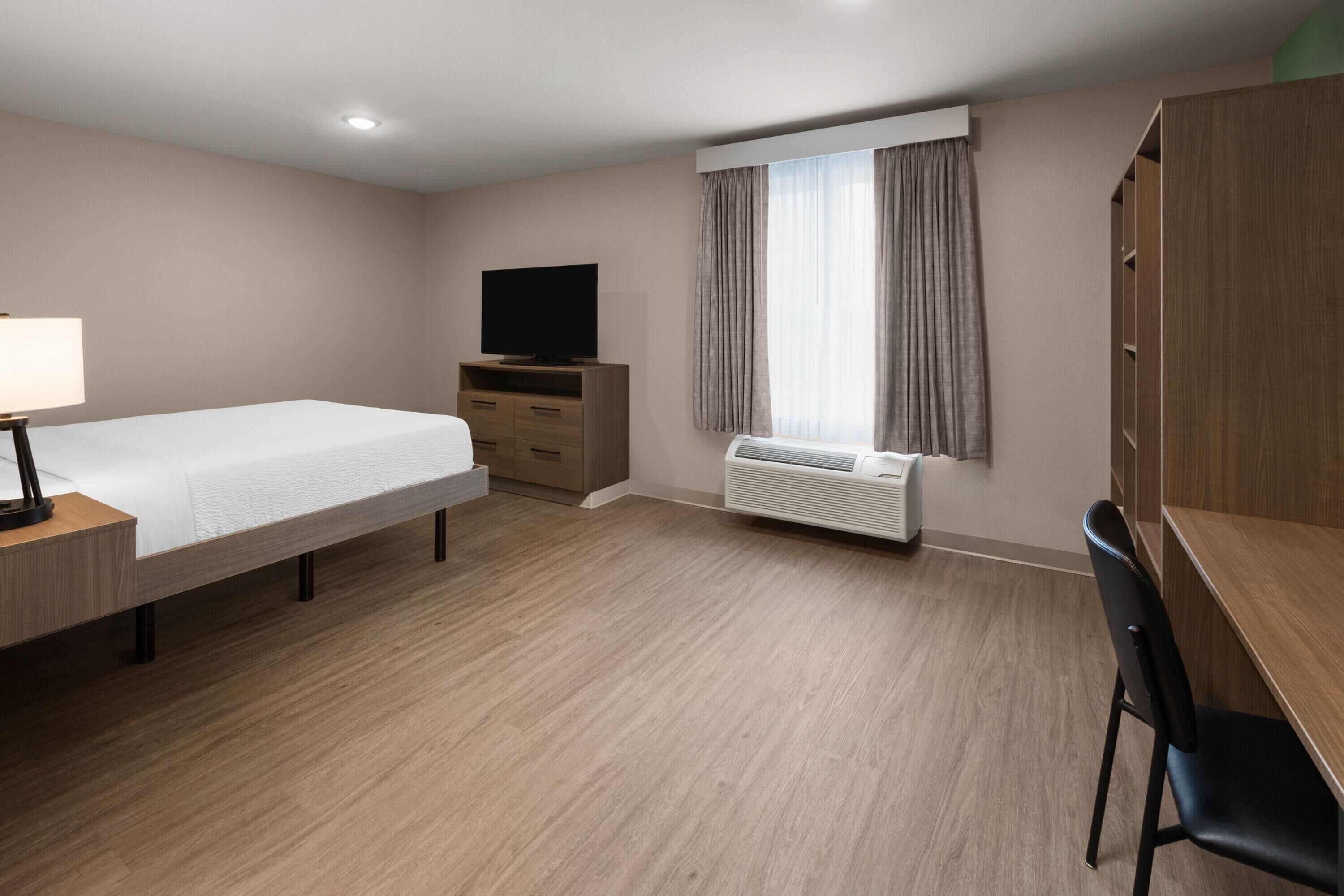 A hotel room with a bed, a desk with a lamp, a television, a wardrobe, and a window with curtains.